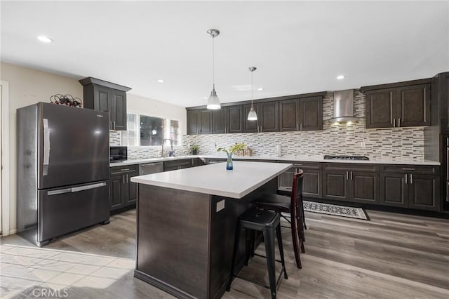 kitchen featuring gas stovetop, light countertops, freestanding refrigerator, wall chimney range hood, and dark brown cabinets