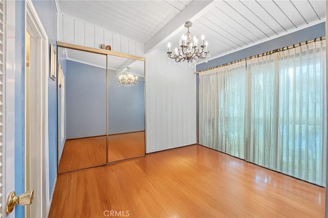 unfurnished bedroom featuring a closet, beamed ceiling, an inviting chandelier, and wood finished floors