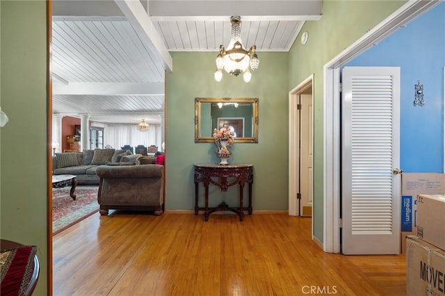 hall featuring ornate columns, wood finished floors, beam ceiling, and a notable chandelier