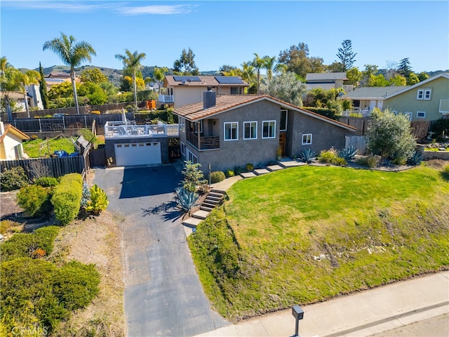 view of front of home featuring aphalt driveway, fence, roof mounted solar panels, a front lawn, and stucco siding