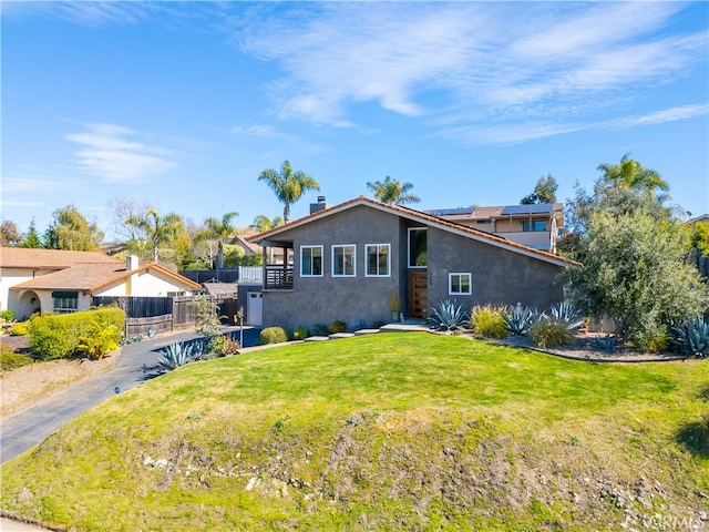 view of front of home with roof mounted solar panels, a front yard, fence, and stucco siding