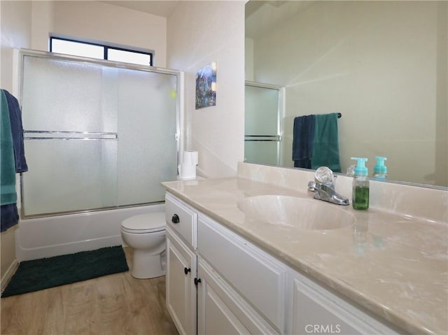 full bath featuring vanity, combined bath / shower with glass door, wood finished floors, and toilet