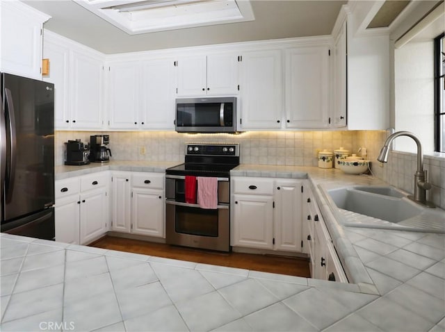 kitchen with tile countertops, stainless steel appliances, a sink, and white cabinets