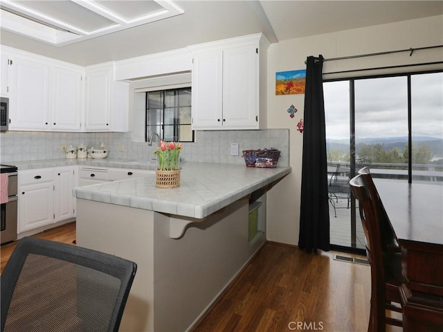 kitchen featuring tile counters, stainless steel microwave, dark wood-type flooring, white cabinetry, and a sink