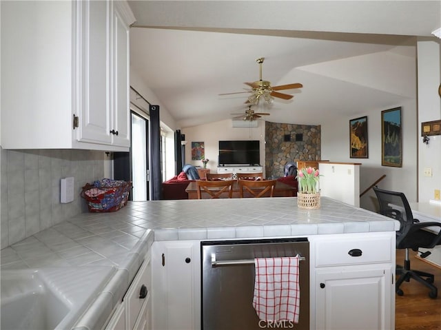 kitchen with tile countertops, a peninsula, vaulted ceiling, and white cabinets