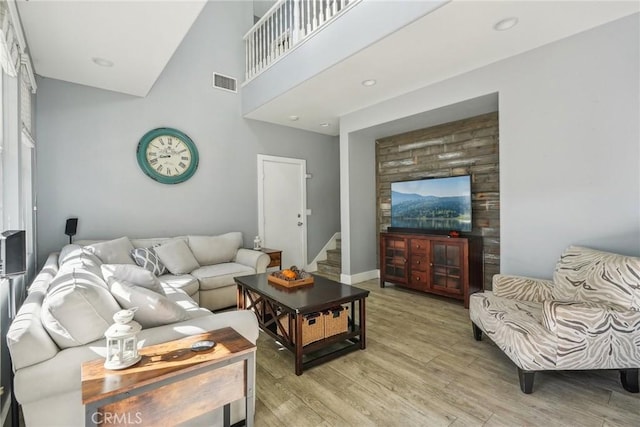 living room with visible vents, baseboards, light wood-style flooring, stairway, and a high ceiling