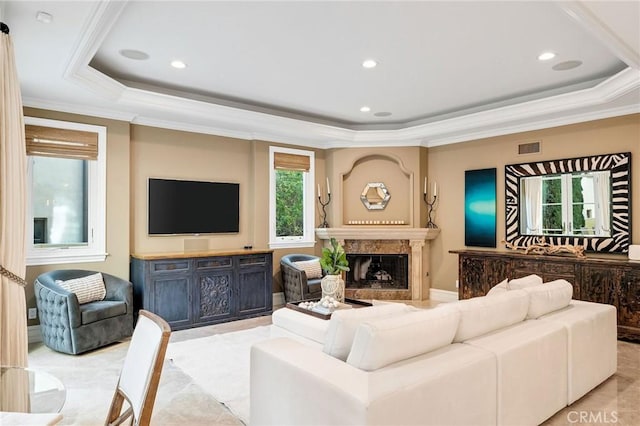 living room featuring a high end fireplace, a tray ceiling, visible vents, and ornamental molding