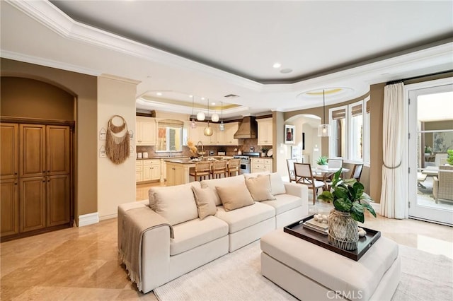 living room featuring arched walkways, a tray ceiling, ornamental molding, and baseboards