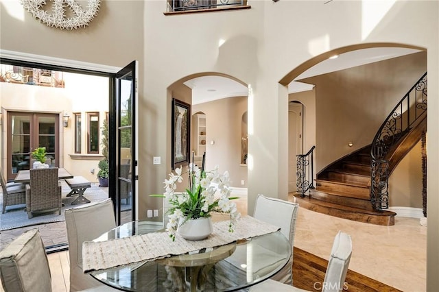 dining room with arched walkways, stairway, a high ceiling, wood finished floors, and baseboards