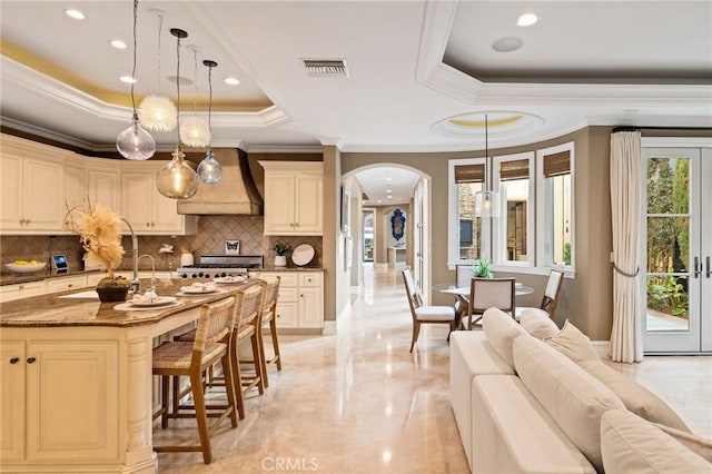 kitchen featuring visible vents, arched walkways, a kitchen breakfast bar, a tray ceiling, and premium range hood