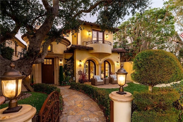 mediterranean / spanish home with a balcony, a tile roof, french doors, a patio area, and stucco siding