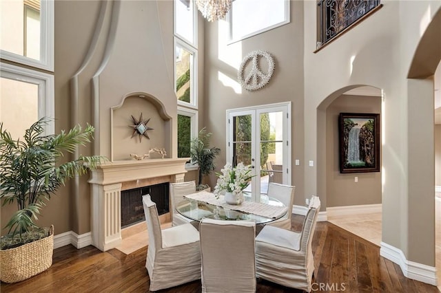 dining room featuring baseboards, a premium fireplace, a high ceiling, and wood finished floors