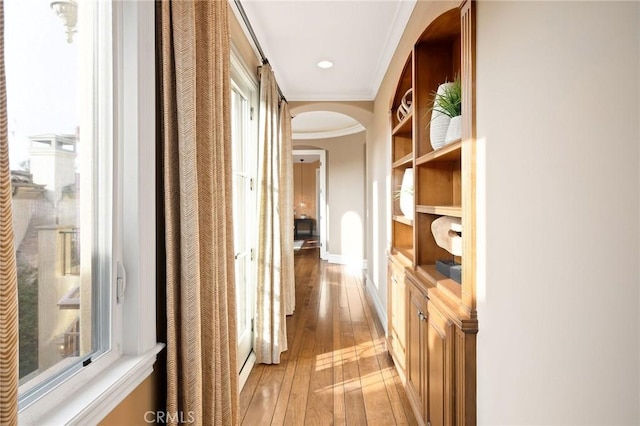 corridor featuring light wood-style floors, baseboards, arched walkways, and crown molding