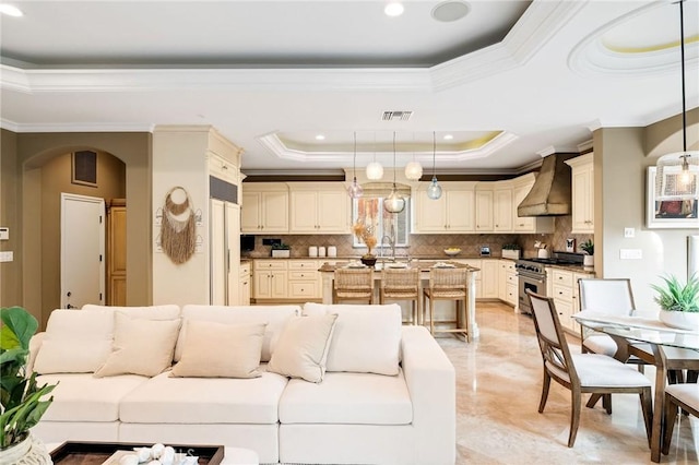 living room featuring a tray ceiling, visible vents, crown molding, and arched walkways