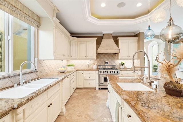 kitchen featuring a tray ceiling, luxury stove, custom range hood, and a sink