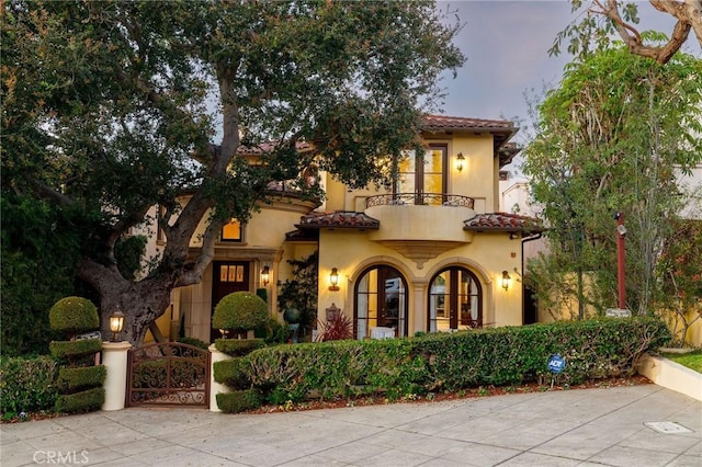 mediterranean / spanish house with a balcony, a tile roof, a gate, and stucco siding