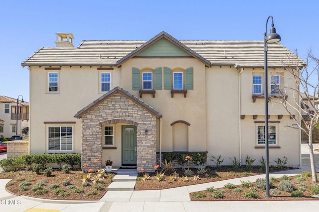 view of front of home featuring stone siding, a tiled roof, a chimney, and stucco siding