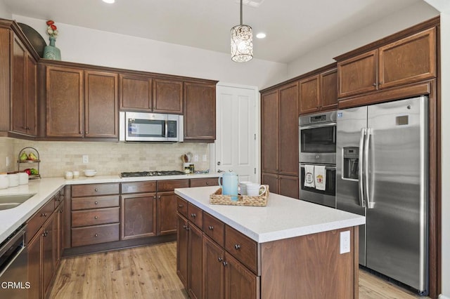 kitchen featuring decorative backsplash, appliances with stainless steel finishes, a center island, light countertops, and light wood-type flooring