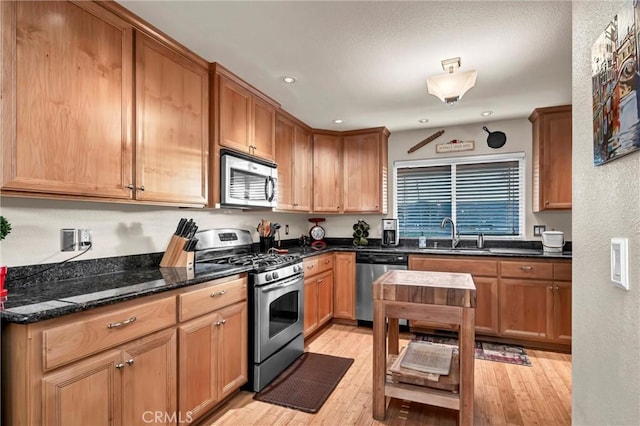 kitchen featuring appliances with stainless steel finishes, dark stone countertops, a sink, and light wood-style flooring