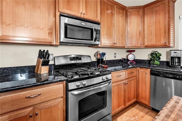 kitchen with stainless steel appliances, dark stone countertops, brown cabinets, and light wood-style floors