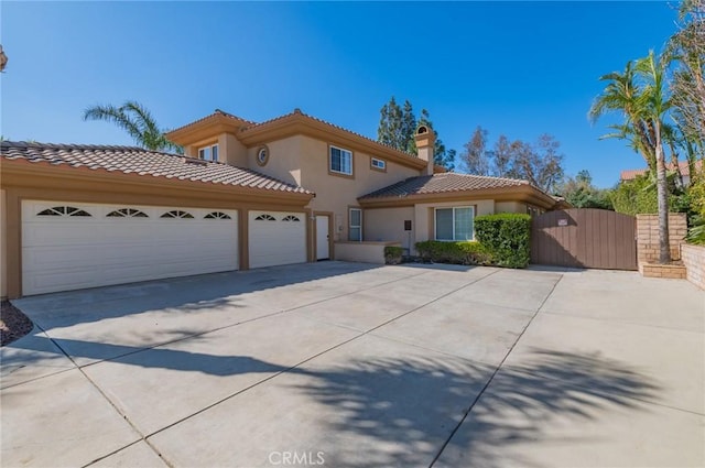 mediterranean / spanish home featuring an attached garage, a tile roof, concrete driveway, a gate, and stucco siding