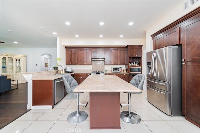 kitchen with light tile patterned floors, stainless steel appliances, a peninsula, a kitchen breakfast bar, and light stone countertops