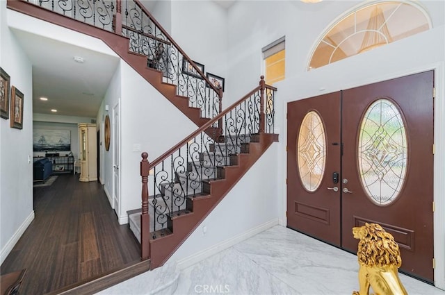 entryway with a towering ceiling, french doors, marble finish floor, and baseboards