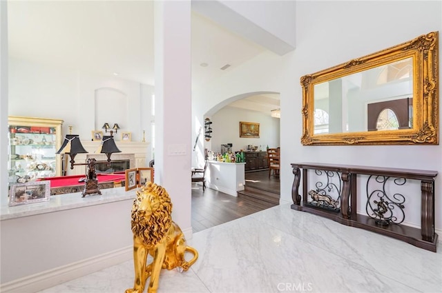 foyer with arched walkways, marble finish floor, and a glass covered fireplace