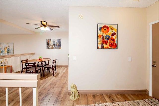 dining area featuring a ceiling fan, baseboards, light wood finished floors, and a textured ceiling