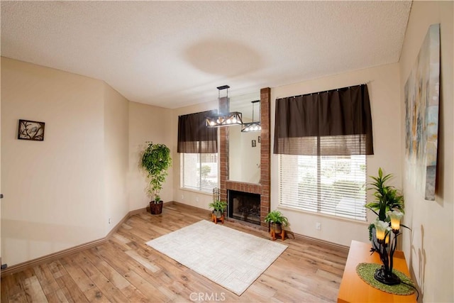 unfurnished living room featuring a brick fireplace, wood finished floors, baseboards, and a textured ceiling