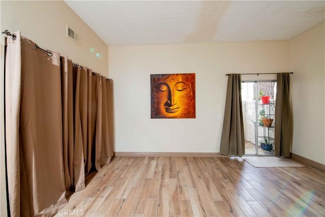 spare room with visible vents, light wood-style flooring, a textured ceiling, and baseboards