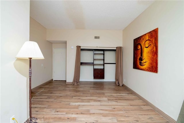 unfurnished room with baseboards, light wood-style floors, visible vents, and a textured ceiling