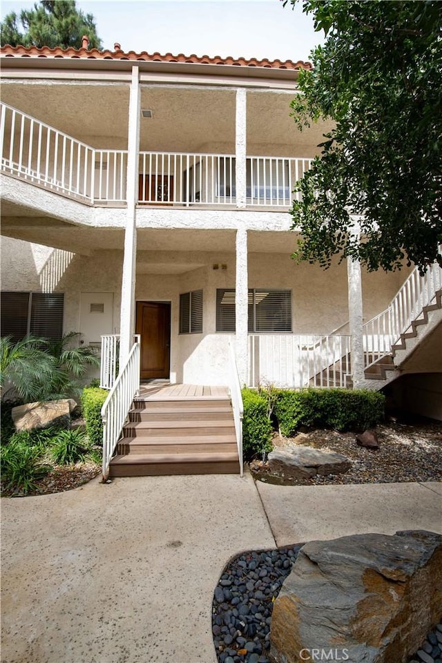 exterior space featuring a porch, stucco siding, a tiled roof, and a balcony