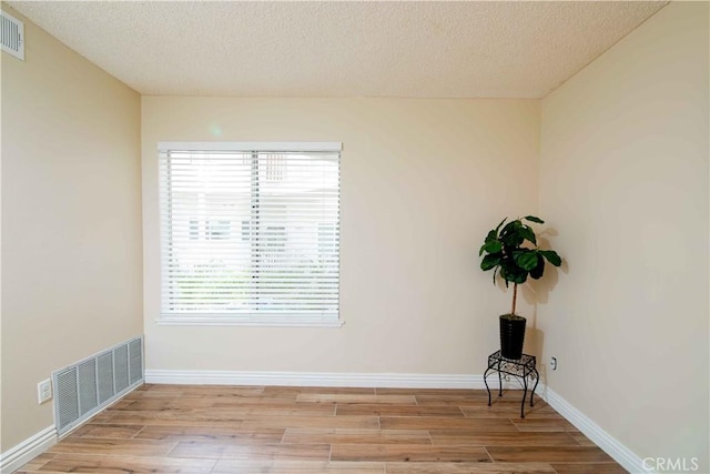 empty room featuring visible vents, a textured ceiling, and wood finished floors