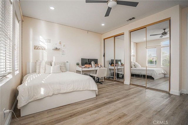 bedroom with ceiling fan, recessed lighting, wood finished floors, visible vents, and two closets