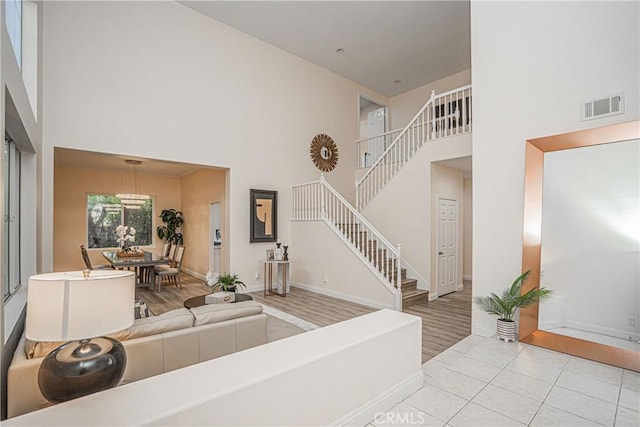 tiled living room with stairway, baseboards, a high ceiling, and visible vents