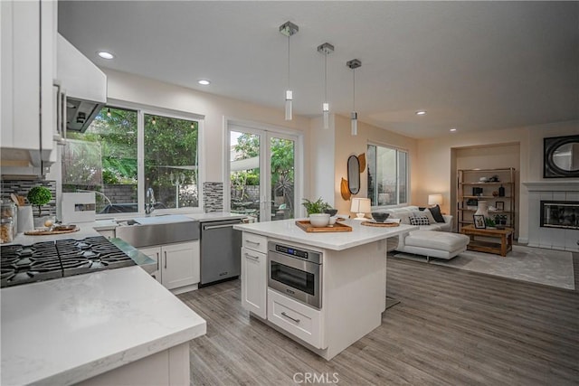 kitchen with light wood finished floors, a glass covered fireplace, open floor plan, white cabinetry, and dishwasher