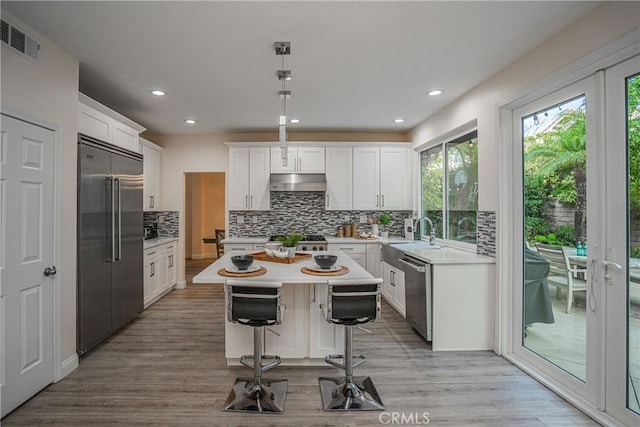 kitchen featuring visible vents, appliances with stainless steel finishes, a center island, light countertops, and under cabinet range hood