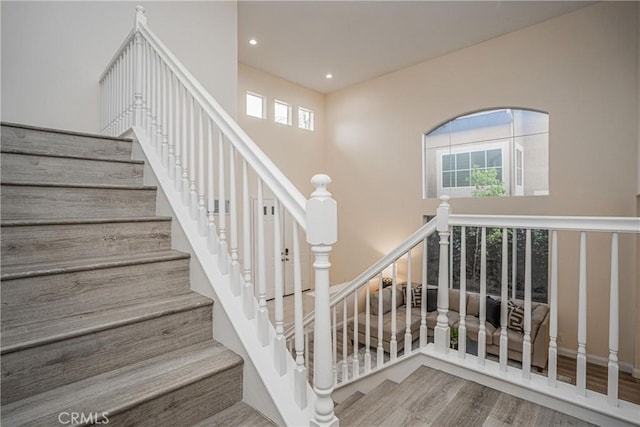 staircase with a towering ceiling, wood finished floors, and recessed lighting