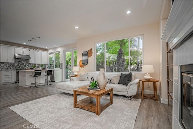 living area featuring light wood-style floors, recessed lighting, a glass covered fireplace, and baseboards