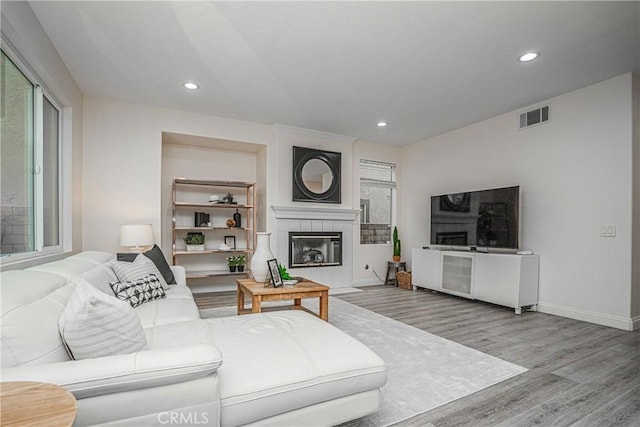 living room featuring a tiled fireplace, wood finished floors, visible vents, and a healthy amount of sunlight