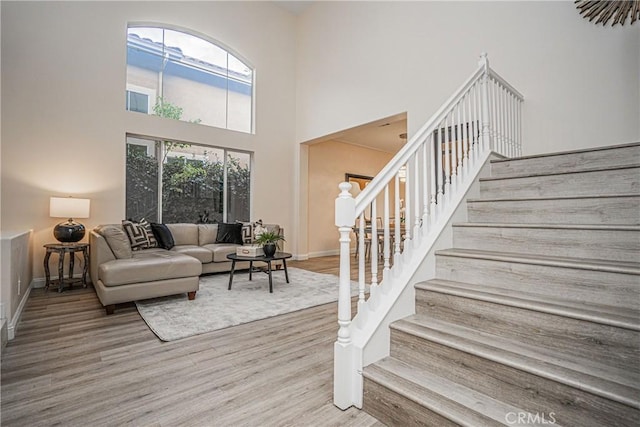 living area featuring baseboards, stairway, a high ceiling, and wood finished floors