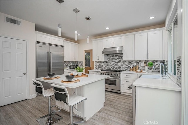 kitchen with visible vents, high end appliances, a center island, under cabinet range hood, and a sink