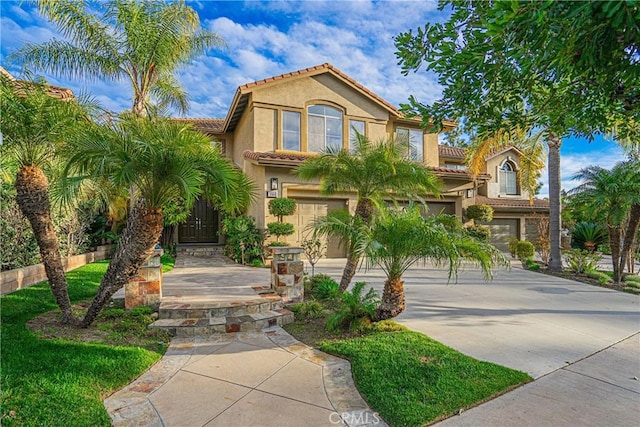 mediterranean / spanish-style house featuring driveway, an attached garage, a tiled roof, and stucco siding