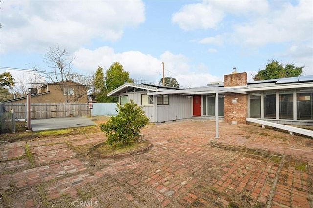 back of house featuring solar panels, a patio, a chimney, and fence