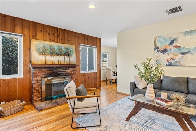 living room with visible vents, wood walls, a fireplace, and wood finished floors