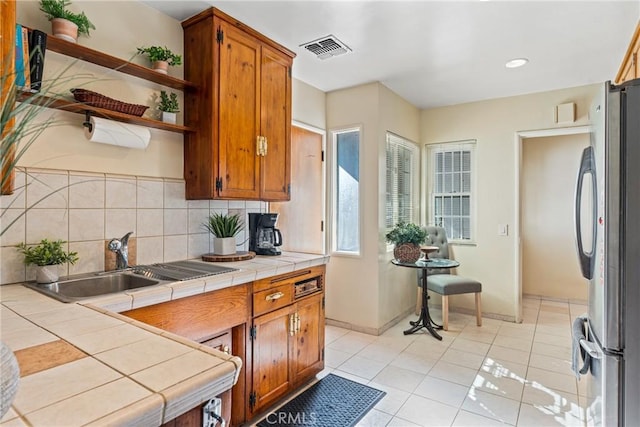 kitchen featuring tile countertops, visible vents, a sink, and freestanding refrigerator