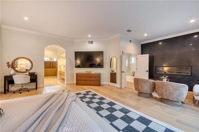 bedroom featuring arched walkways, visible vents, ornamental molding, light wood-type flooring, and ensuite bath