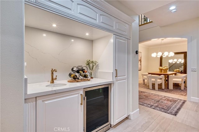 bar featuring arched walkways, wine cooler, crown molding, a chandelier, and a sink