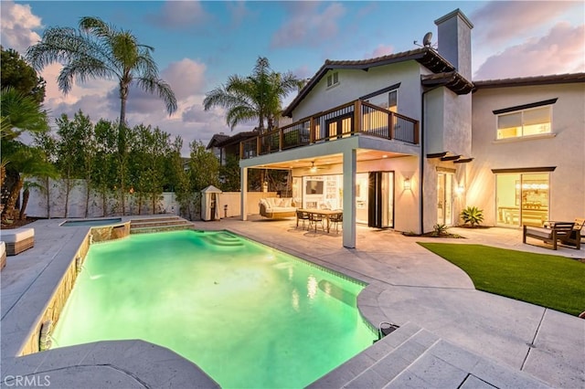 pool at dusk featuring a storage unit, a patio area, a fenced backyard, and an outdoor structure